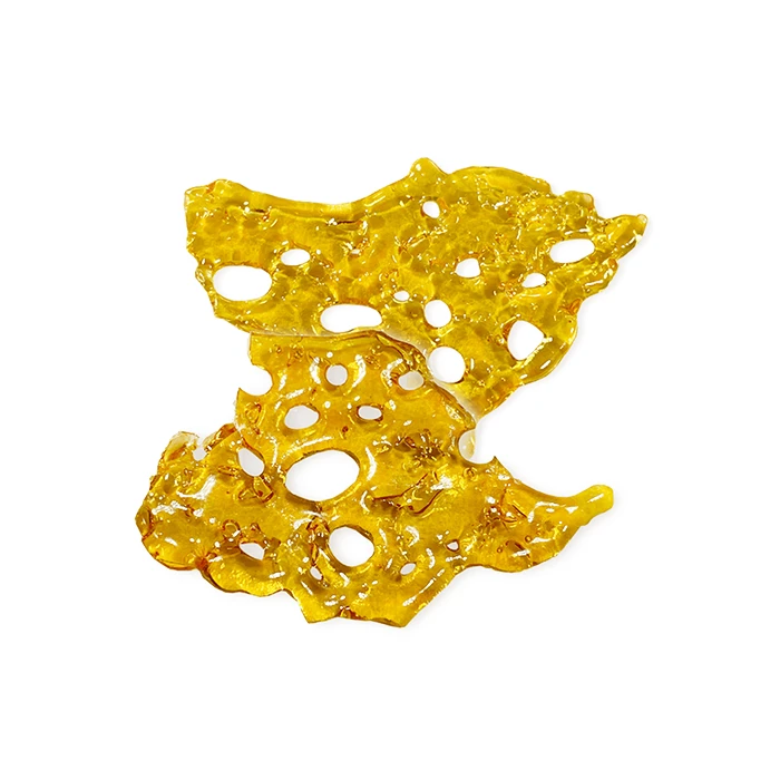 A close-up of a golden, translucent cannabis Diamond Concentrates shatter piece with irregular edges and bubble-like holes scattered throughout.