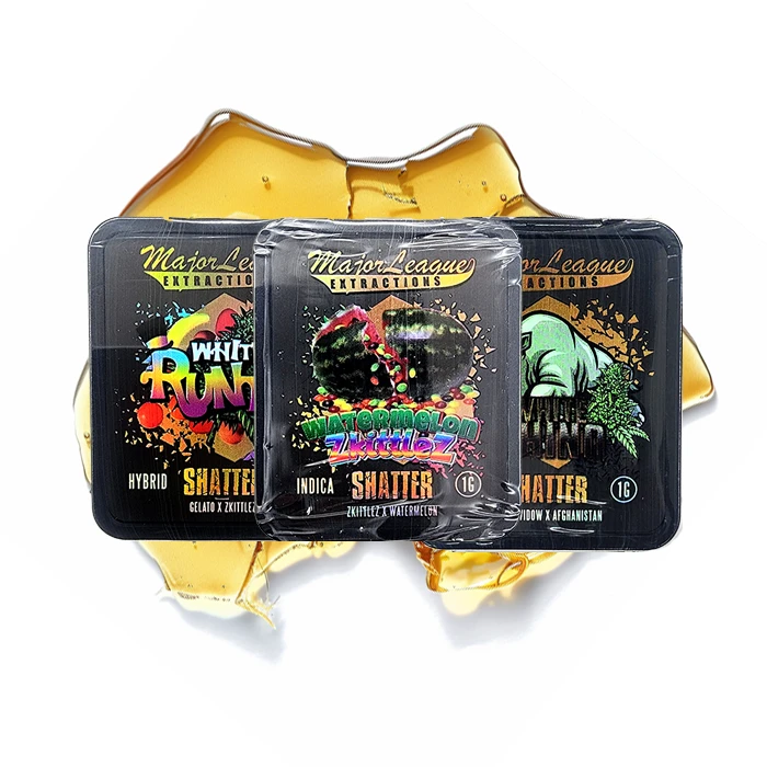 Three Major League Extractions Shatter packages displayed on top of a golden shatter background. The strains shown include White Runtz, Watermelon Zkittlez, and White Widow x Afghanistan.