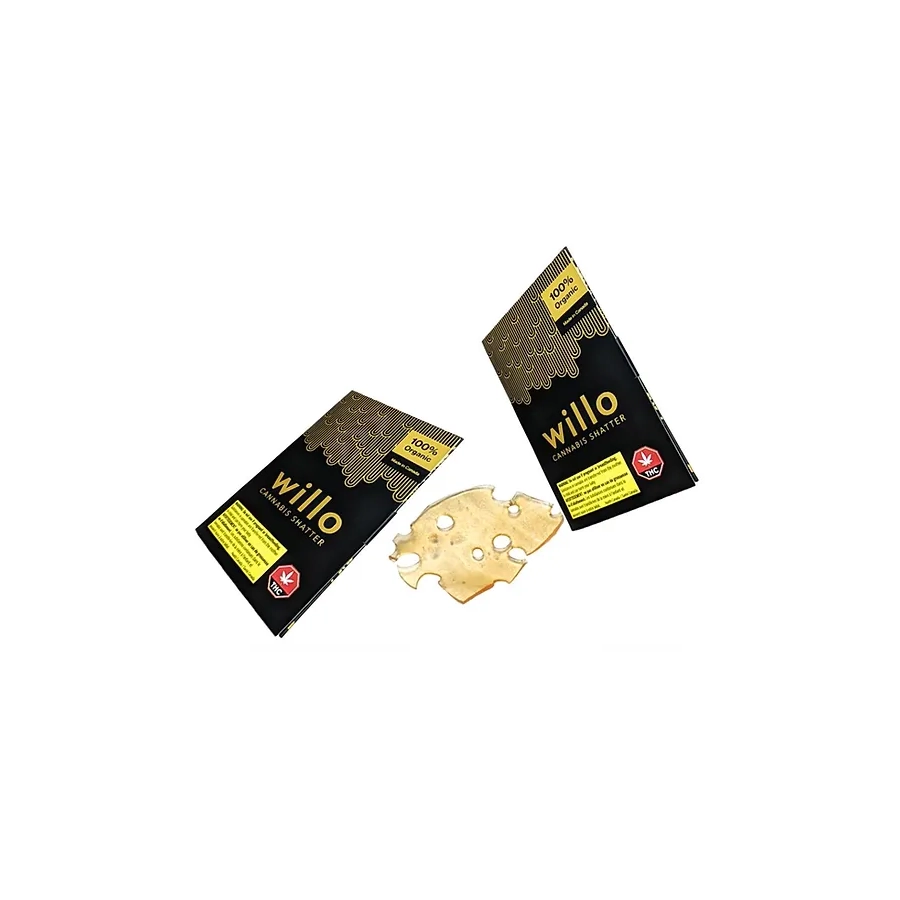Two black and gold packages of Willo Cannabis Shatter placed side by side, each displaying the 100% organic label. Between the packages is a translucent piece of cannabis shatter with a honey-like appearance.