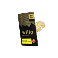 A black and gold package of Willo Cannabis Shatter, featuring 100% organic labeling and Canadian cannabis warnings. The package is partially open, showing a piece of translucent, golden cannabis shatter.