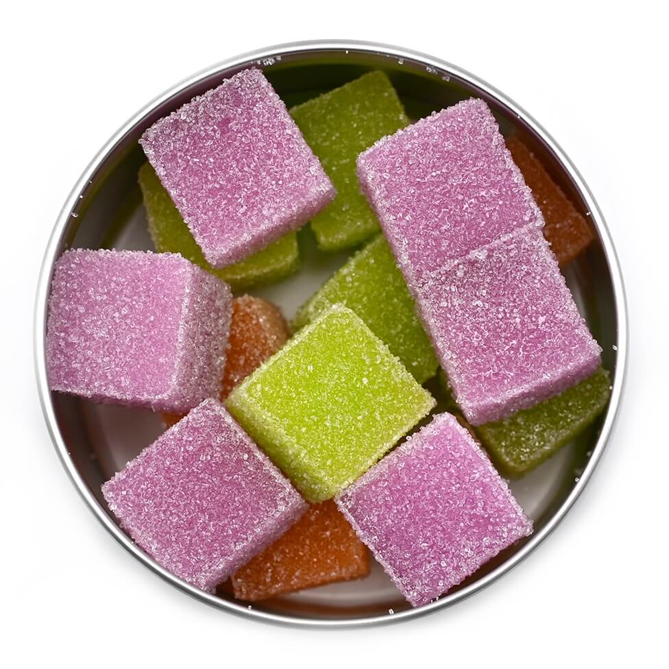 A top-down view of Bliss Party Mix square-shaped gummies in purple, green, and orange colors, arranged in an open tin