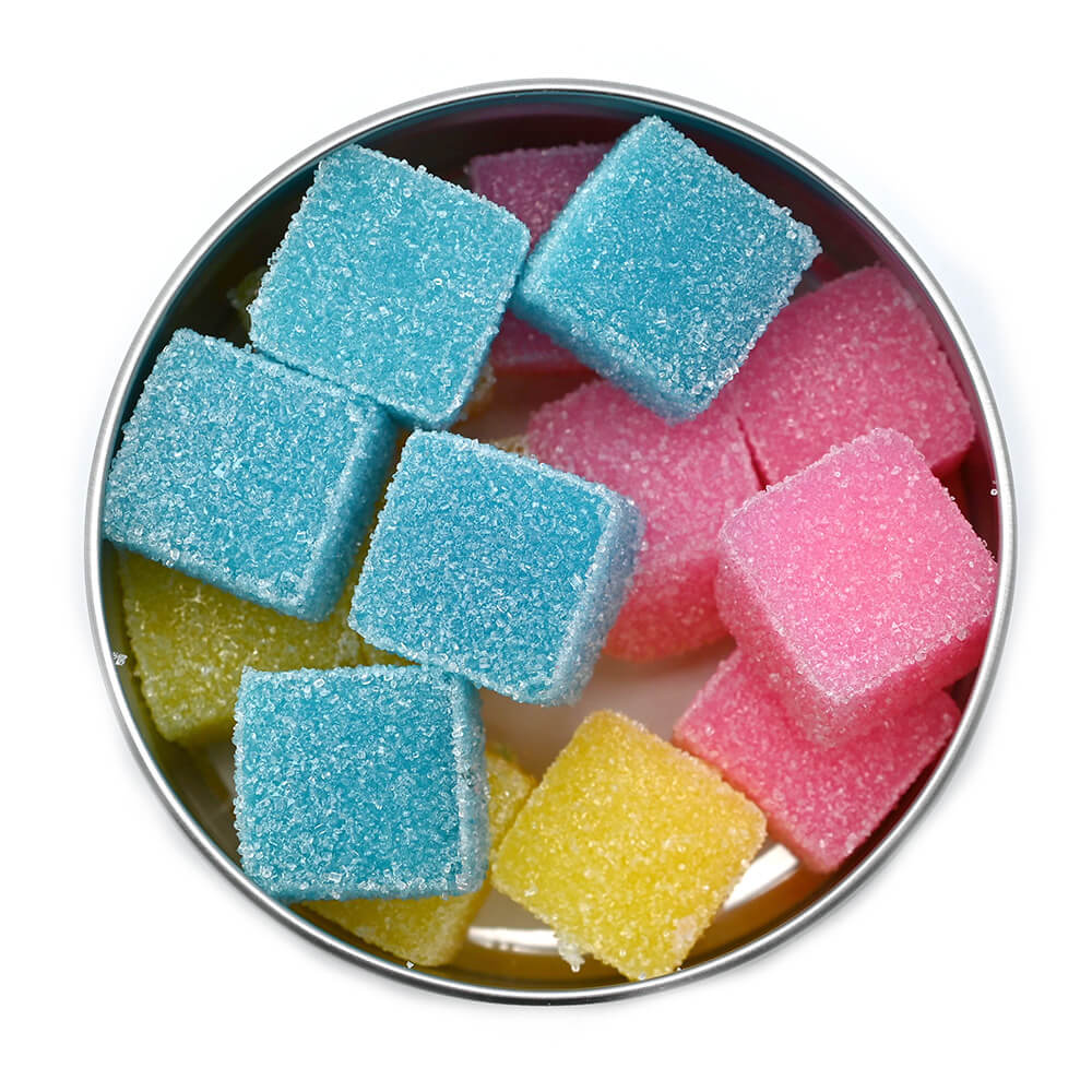 A top-down view of square-shaped cannabis-infused gummies in blue, pink, and yellow flavors, neatly arranged in an open tin