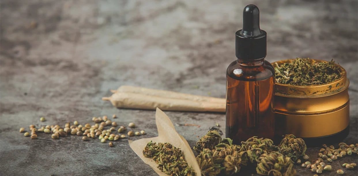 Various cannabis products including a dropper bottle, cannabis buds, rolling papers, and seeds displayed on a rustic surface. This image represents Weed Market, an online dispensary in Canada, offering a wide range of cannabis products