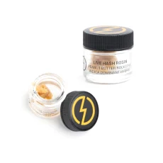 A glass jar of High Voltage Extracts Hash Live Rosin, labeled "Peanut Butter Rockstar, Indica Dominant Hybrid," with the jar opened to display the golden, smooth concentrate inside. The black jar lid, featuring a yellow lightning bolt logo, is positioned beside the jar.