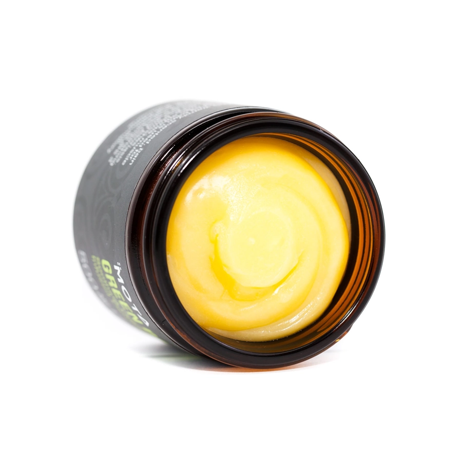 A close-up of MOTA Green Balm 2oz, displaying the smooth yellow ointment inside the jar, emphasizing its creamy and soothing texture