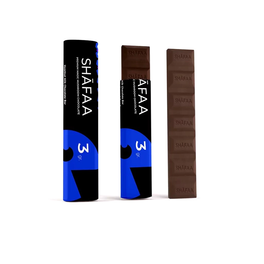Shafaa Penis Envy Mushroom Milk Chocolate Bar packaging with a blue and black label featuring the product name and '3g' marking. The bar is displayed with six breakable chocolate squares embossed with the Shafaa logo