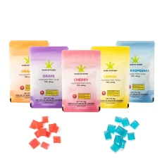 Kush Kitchen Hard Candy Variety Pack featuring orange, grape, cherry, lemon, and blue raspberry flavors in colorful packaging with THC 150mg, displayed with red and blue hard candy pieces on a white background.
