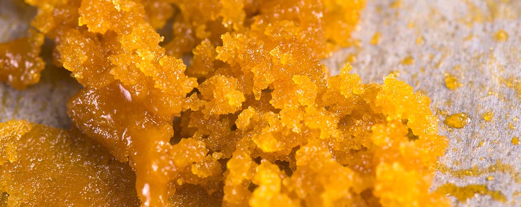 Macro shot of HTFSE concentrate spread across parchment paper, highlighting its vibrant orange color and textured appearance at Weed Market.