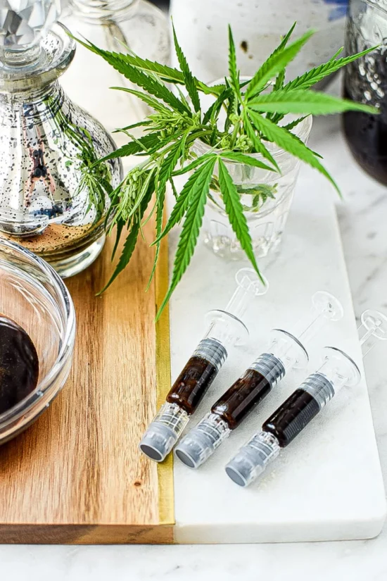 Plastic syringes filled with dark cannabis oil next to fresh cannabis leaves, representing Phoenix Tears Online medical cannabis products.