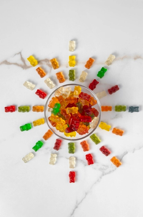 A glass bowl filled with colorful weed gummies arranged in a sunburst pattern on a white marble surface, showcasing a fun and vibrant edible presentation.