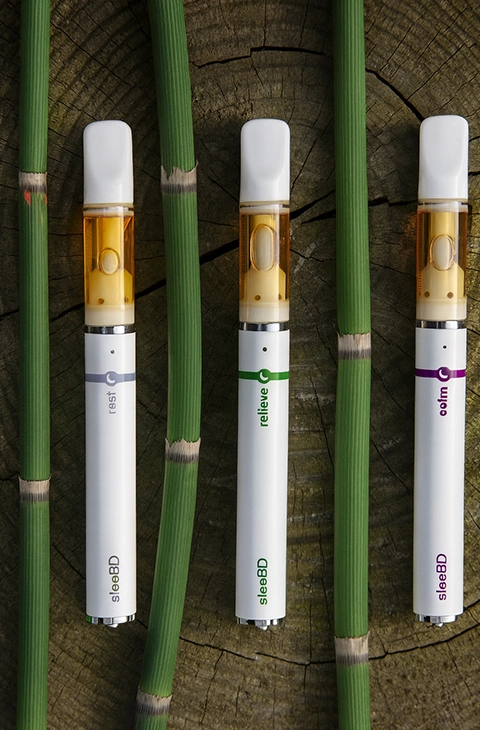SleeBD vape pens Rest Relieve Calm arranged on wooden surface with green stems