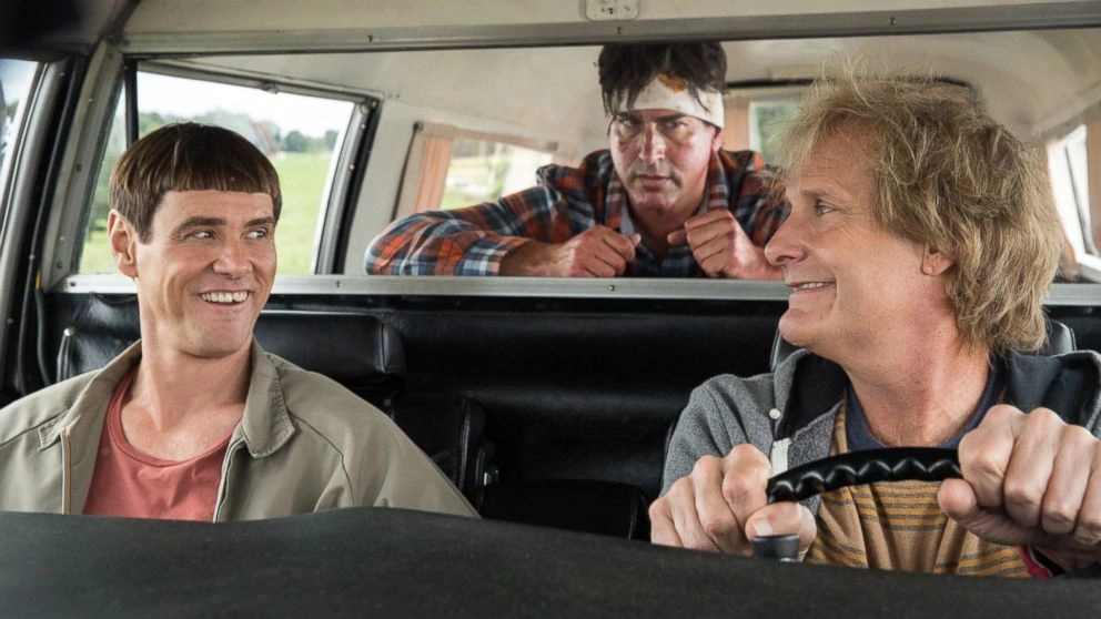 Jim Carrey and Jeff Daniels sit in the front of a van while a bandaged man leans in from behind in Dumb and Dumber To