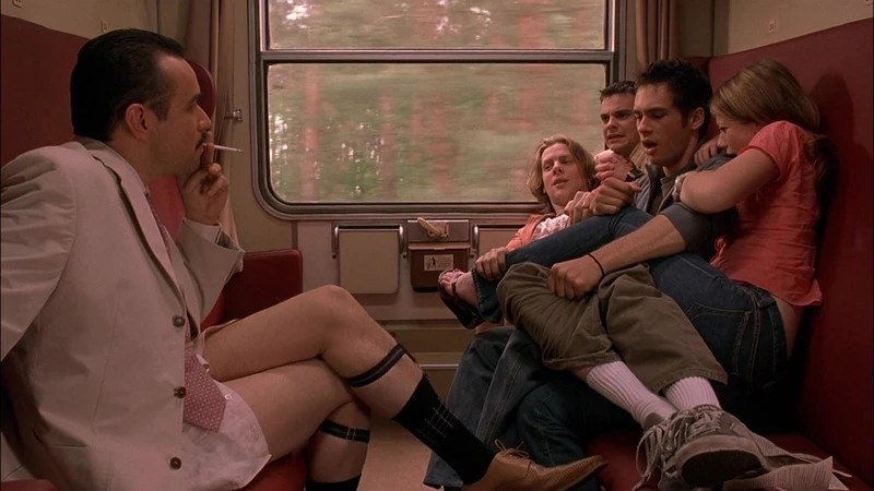 Three young men and a woman crowd onto a train seat beside a man in a suit smoking in Eurotrip