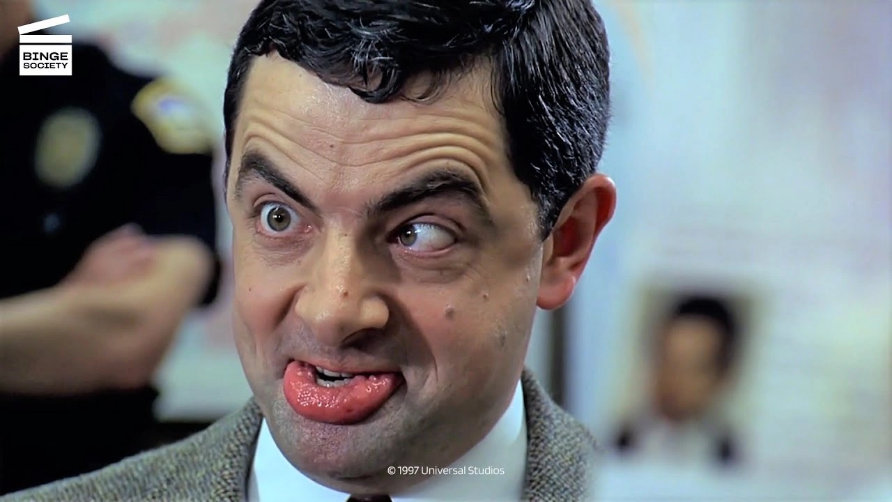 Rowan Atkinson pulls a wide-eyed cross-eyed face with his tongue out as Mr Bean